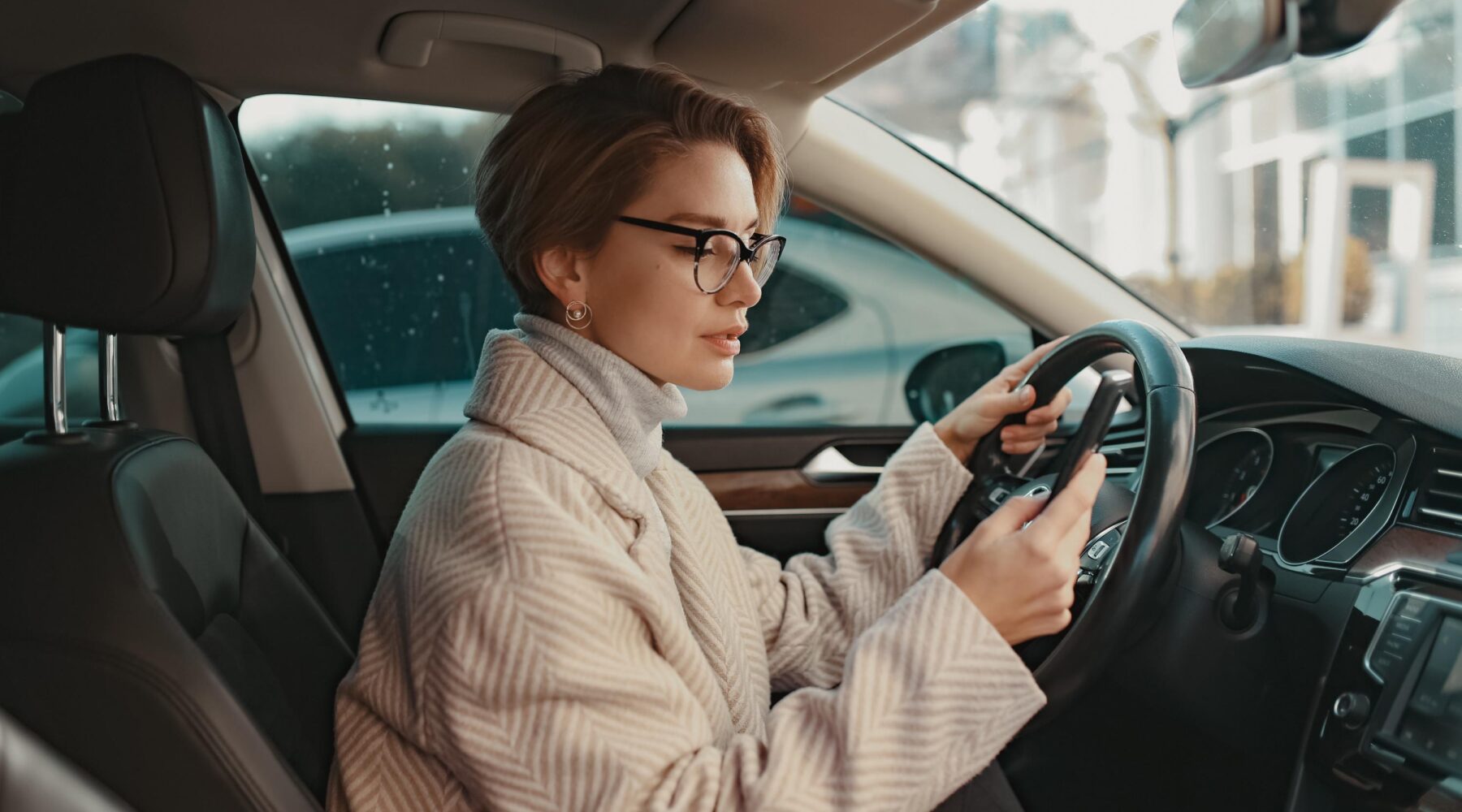 Frau im Auto hinter dem Steuer mit Handy in der Hand.